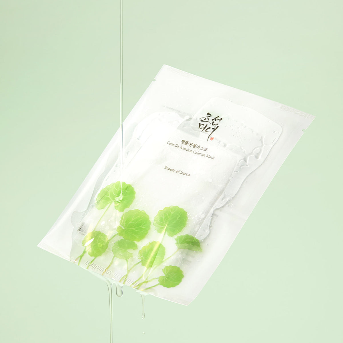 Beauty of Joseon Centella Asiatica Calming Mask sachet with green leaf illustrations, tilted with water flowing over it.